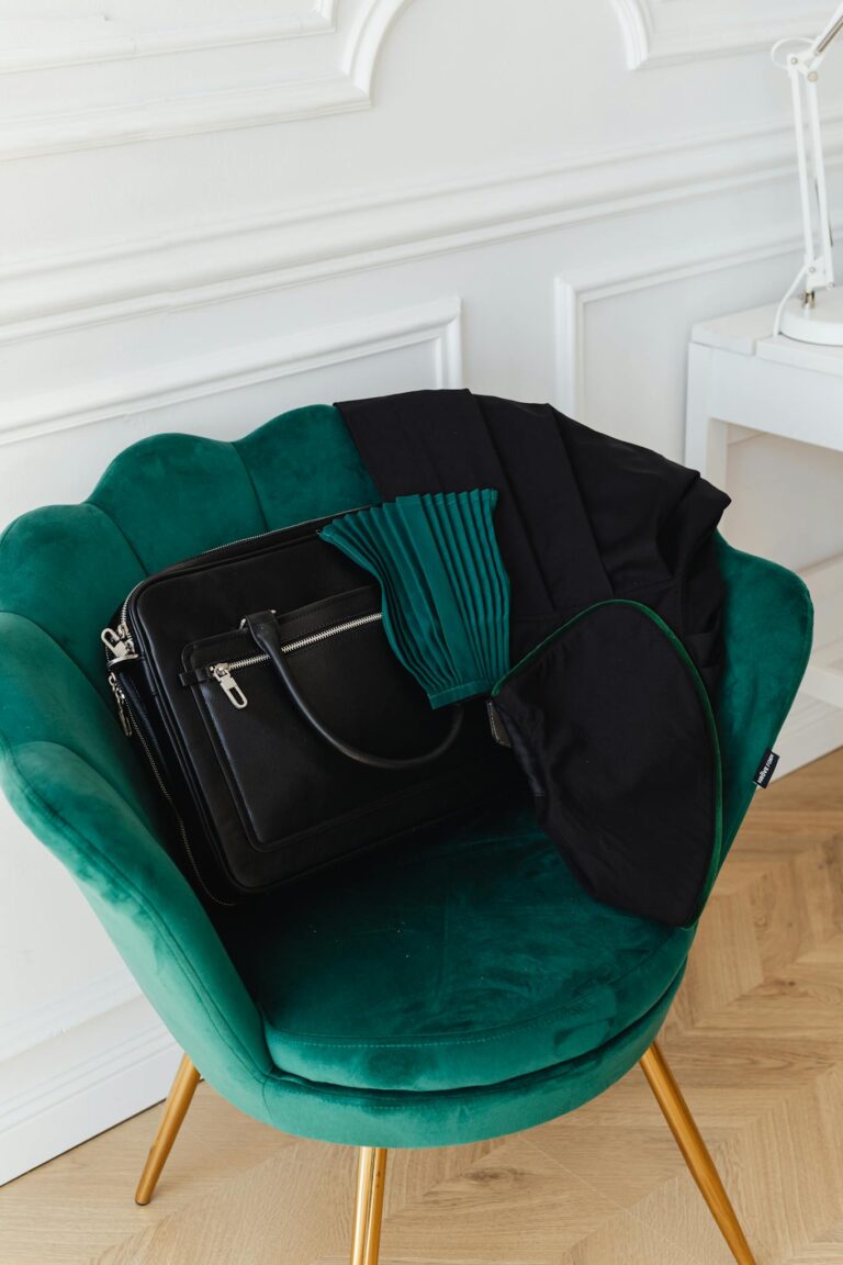 Elegant green velvet armchair with a black leather bag and scarf in a contemporary interior setting.